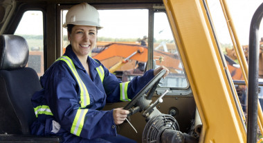 Female construction worker sits in a digger and smiles at the camera.