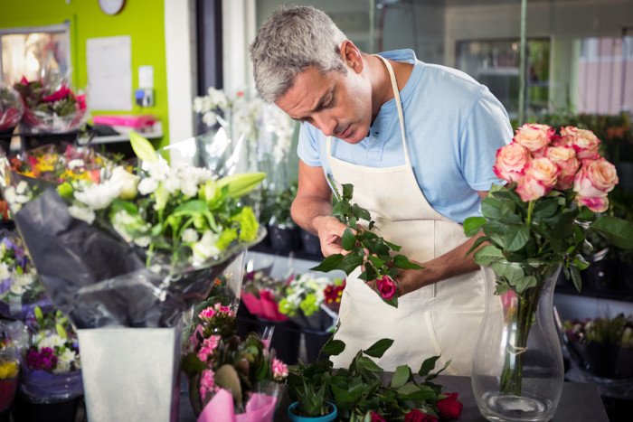 A male florist arranging roses into a bouquet