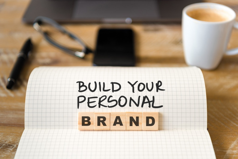A notebook with text saying that says build your personal brand next to a cup of coffee