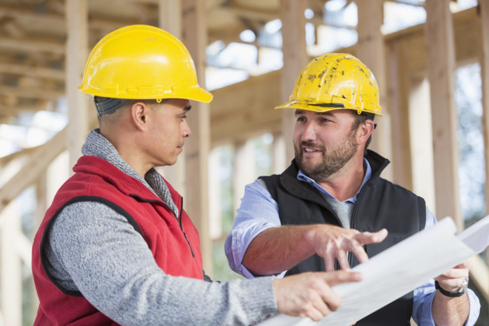 Building contractor holding a building plan and talking to a construction worker