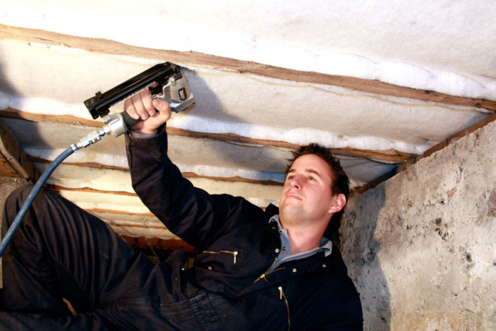 A building insulator stapling insulation to the underside of a floor