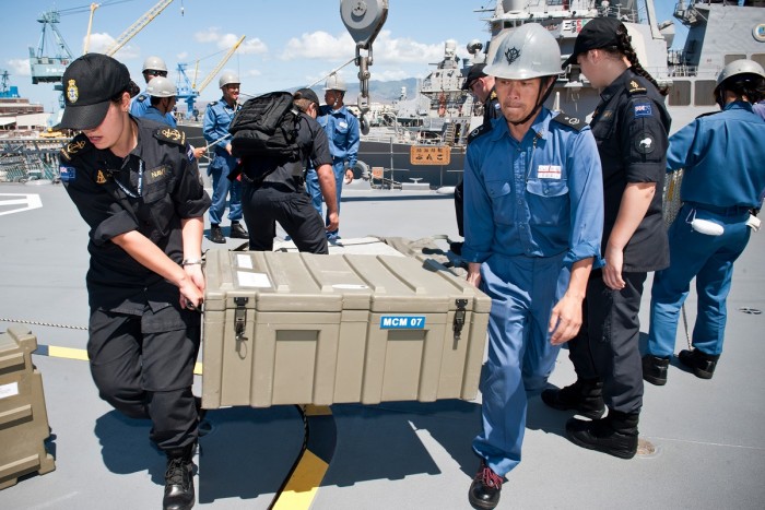 A NZ female sailor and a Japanese male sailor lift cargo off a Japanese naval frigate in a joint exercise