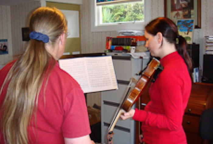 Susan Case and a student holding a violin look at a piece of music on a music stand