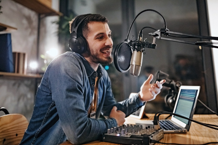 A male radio presenter talking into a microphone in a broadcasting studio