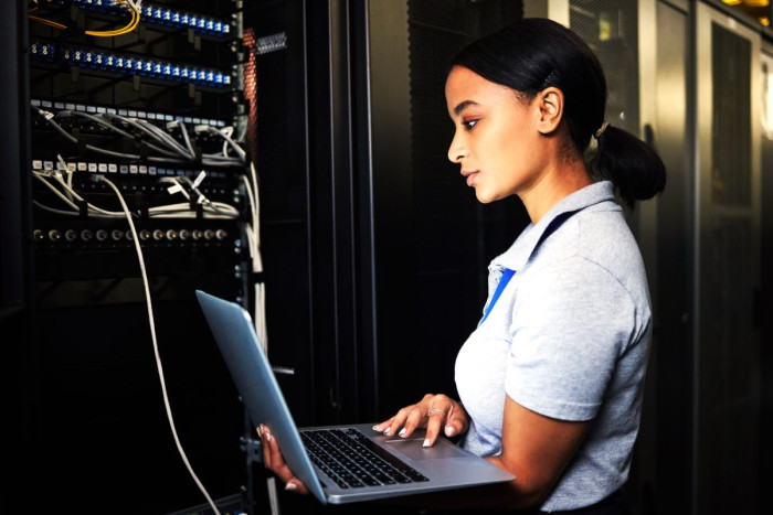 A woman uses a laptop in a server room 