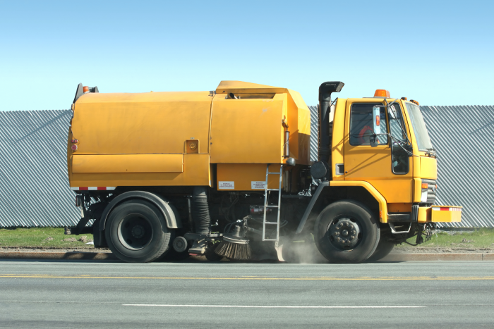 Street/park cleaner operates a yellow streetsweeping truck to clean gutters